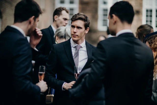 Mens cocktail attire UK shown on men in dark suits at an evening event